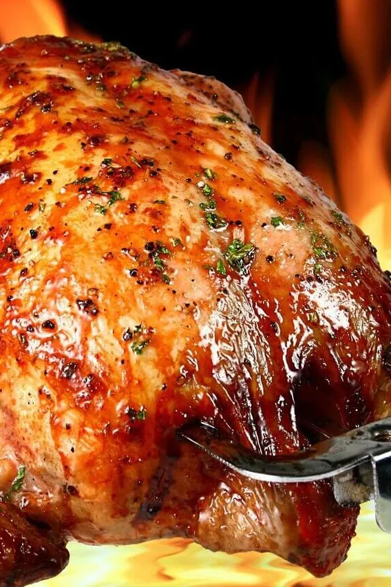 A whole chicken roasting on a spit in front of open flames